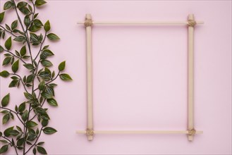 Wooden square frame with artificial green leaves pink backdrop