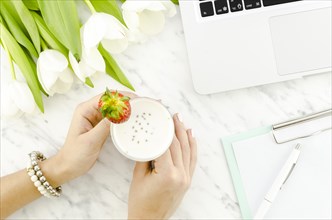 Woman holding yogurt drink near laptop