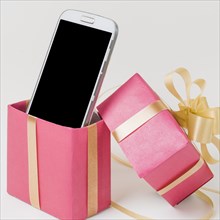 Close up cellphone decorated pink gift box against white surface