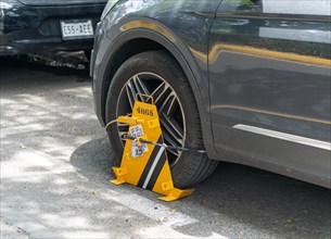 Car clamp fixed to front wheel of car parked on street