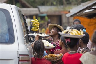 Local Malagasy women selling bananas and food to passers-by traveling in vehicle in rural village in Madagascar