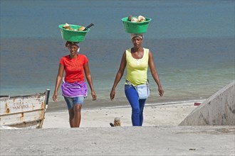 Two Creole women carrying plastic tubs with coconuts out of the harbour of Tarrafal on the island Santiago