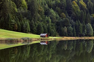 Wooden hut and reflection of pine forest in water along lake Gerold