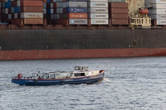 The barge Nordsee IV in front of a container ship with containers of the shipping company Maersk during a harbour tour in the evening light on the river Elbe in the port of Hamburg