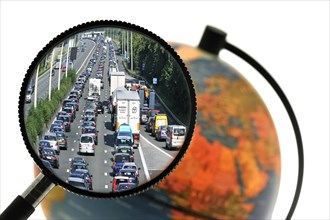 Cars in traffic jam on motorway during the summer holidays seen through magnifying glass held against illuminated terrestrial globe