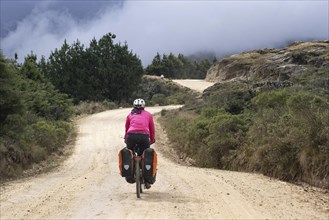 Female cyclist riding heavily laden bicycle with big panniers on dirt road through the Andes mountains