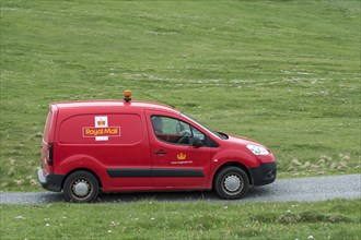 Postman driving red Peugeot Partner Royal Mail post van along desolate road in Shetland