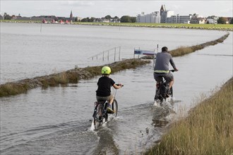 Cyclist on flooded shore path at high tide on the beach of Cuxhaven