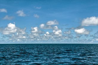 Photo with slightly reduced saturation changed hue of clouds Altocumulus reflected in front of blue sky on horizon over Pacific Still ocean with no waves with in mirror smooth sea surface water surfac...