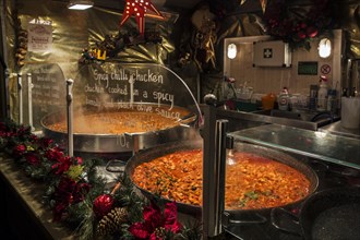 Large pans with simmering spicy chilli chicken for sale in stall during evening Christmas market in winter