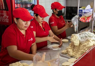 Woman rolling corn dough to make tortillas in gordita fast food cafe restaurant
