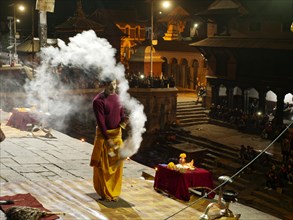Hindu priest performing a ritual with smoke at night in front of the Pashupatinath temple
