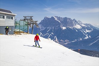 Snowboarder starts on the panoramic run with a view of the Zugspitze