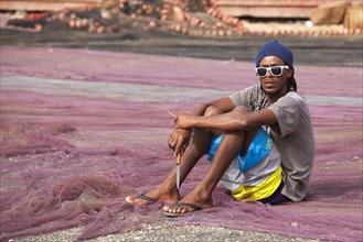 Creole fisherman mending fishing nets in the harbour of the fishing village Palmeira on the island of Sal
