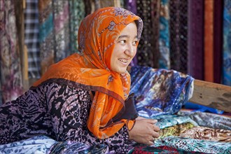 Kyrgyz woman with golden teeth selling colourful fabrics at market in Osh