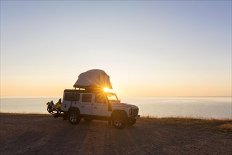 Off-road four-wheel drive vehicle with rooftop tent camping along the Baltic Sea at sunrise in summer