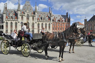 The neo-gothic Provincial Court and tourists in horse-drawn carriage for sightseeing tour at the Market square