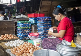 Burmese woman selling eggs and counting money at food market in Yangon