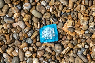 Sachet of 'Add Some Sweet and Sour sauce' washed up on shingle beach