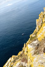 Fishing trawler boat far below steep cliffs Isla del Faro