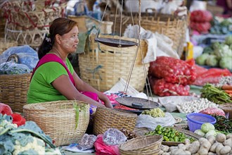 Burmese woman wearing thanaka on her face selling vegetables at food market in village along Inle Lake