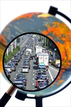 Cars in traffic jam on motorway during the summer holidays seen through magnifying glass held against illuminated terrestrial globe