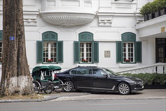 Rickshaws versus luxury car in front of colonial hotel in the capital city Hanoi