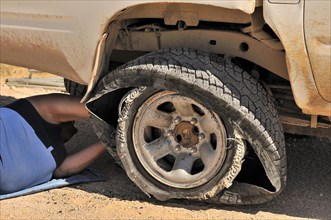 Driver fixing blowout tire of four-wheel drive vehicle in the Namib desert