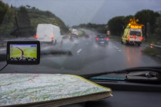 Speeding van overtaking cars on highway during heavy rain shower seen from inside of vehicle with GPS and road map on dashboard