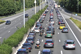 Cars and motorcyclists queueing in highway lanes at approach slip road during traffic jam on motorway during summer holidays