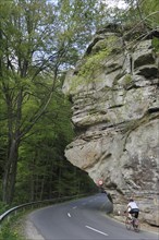 Cyclist riding under the sandstone rock formation Predigtstuhl in Berdorf