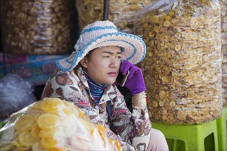 Cambodian woman making a phone call with smartphone while selling dried banana chips at food market in Cambodia