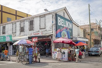 Customers shopping in busy street with shops and market stalls selling fruit in Belize City