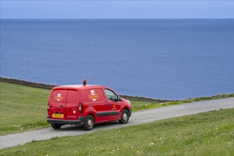 Postman driving red Peugeot Partner Royal Mail post van along desolate coastal road in Shetland