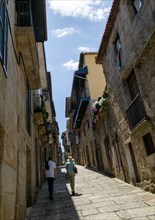 Two people walking past houses on steep narrow street in medieval town