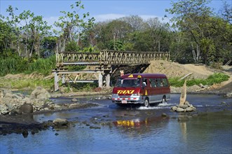 Taxi crossing river by driving through water next to unfinished bridge in Costa Rica