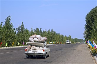 Car overloaded with large sacs stored on roof and in trunk driving along motorway in Uzbekistan