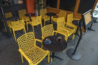 Seating area with yellow chairs and bistro tables in front of a cafe