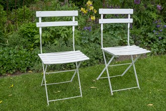 Two white garden chairs in front of a perennial bed