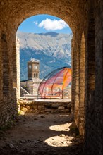 Arches of the fortress of the Ottoman castle of Gjirokaster or Gjirokastra and in the background the church with the clock tower. Albania