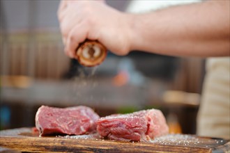 Closeup view of unrecognizable man seasoning raw beef steak with pepper