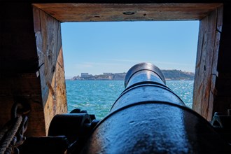Sea view out of a gunport in hull of the ship over the gun cannon muzzle in on the gun deck of a sailing ship of Age of Sail