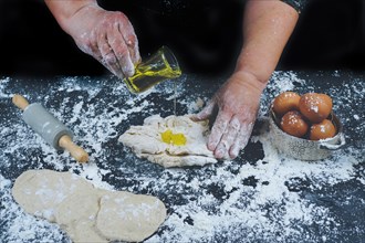 Woman adding olive oil to a flour dough to make homemade bread on a black wooden table with olive oil
