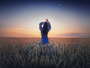 Girl in the golden wheat field at sunset. Beautiful twilight scenery under the summer starry sky with crescent moon. Magical natural scene