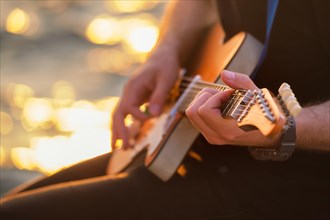 Street musician playing electric guitar hands with guitar pick close up with water in background