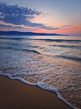 Dawn at the sea with foamy waves on the sand and colorful sky at the horizon. Sunny Beach coastline in Bulgaria. Summer and travel background
