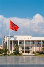 Palace of Culture or Opera on Skanderbeg Square in Tirana and the flag of Albania moving in the wind