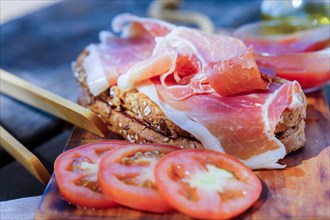 Close-up of a typical Spanish ham and tomato toast on a wooden board with a bowl of freshly crushed tomatoes
