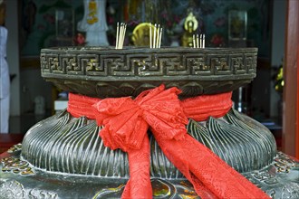 Red ribbon on a bowl for incense sticks in front of a pagoda
