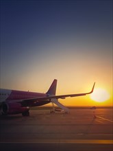 Airplane ready for boarding and takeoff at the airport with the view to the sunrise. Morning travel and holiday concept